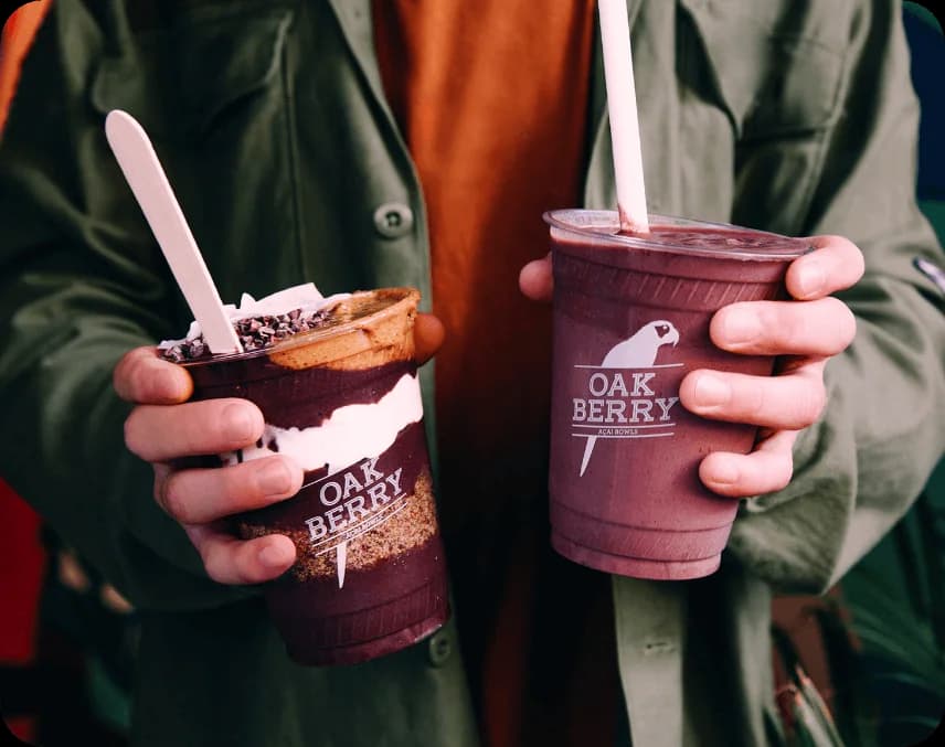 A person holding an OAKBERRY smoothie and an OAKBERRY bowl